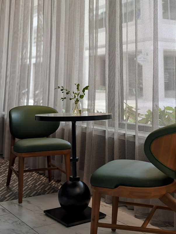 A serene Intercontinental hotel seating area with green upholstered chairs, a small round table, and sheer curtains softly diffusing the daylight
