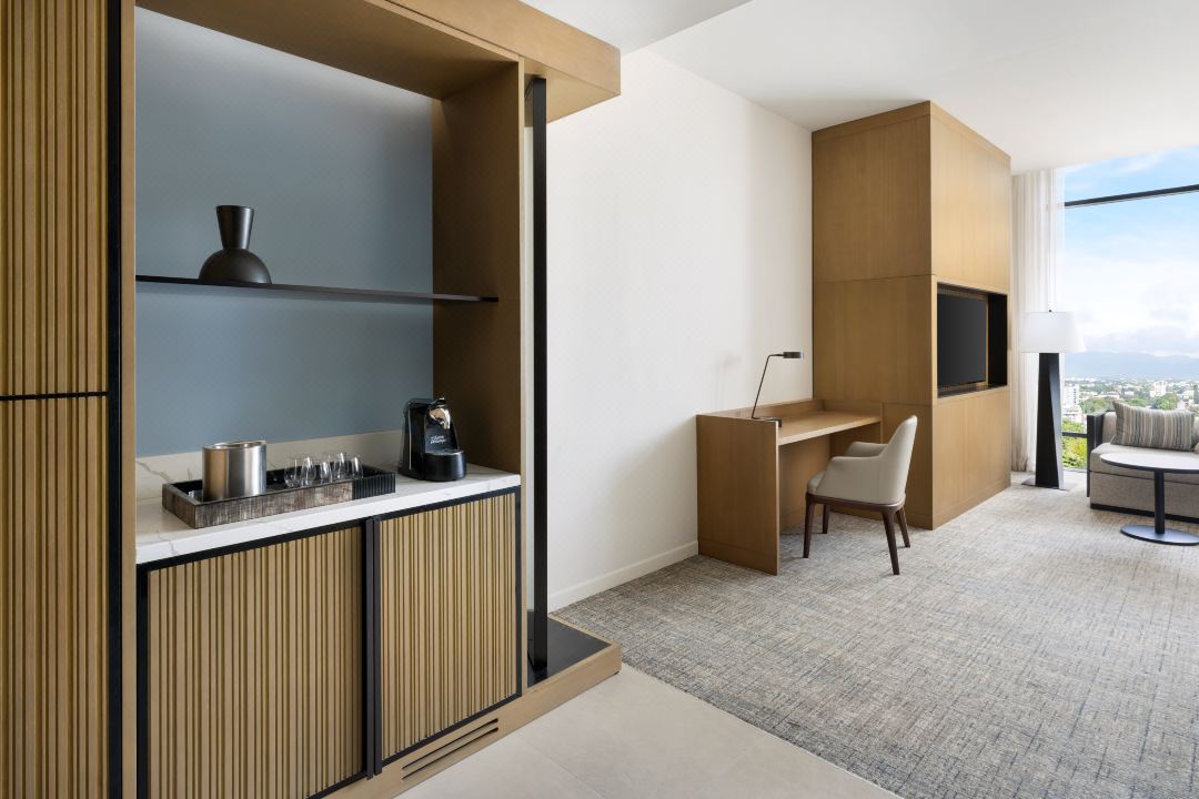 A modern Hilton hotel room with a bar area, desk, and a view of the city through a large window.